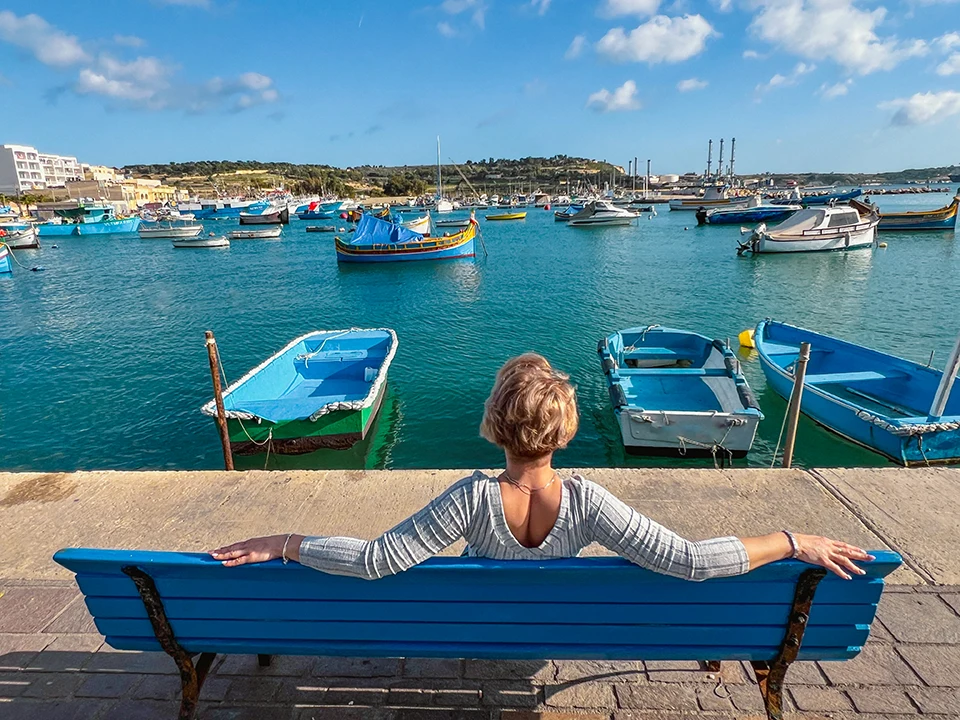 Malta - mulher-sentada-no-banco-e-olhando-para-barcos-em-mar © Viaje Sem Stress